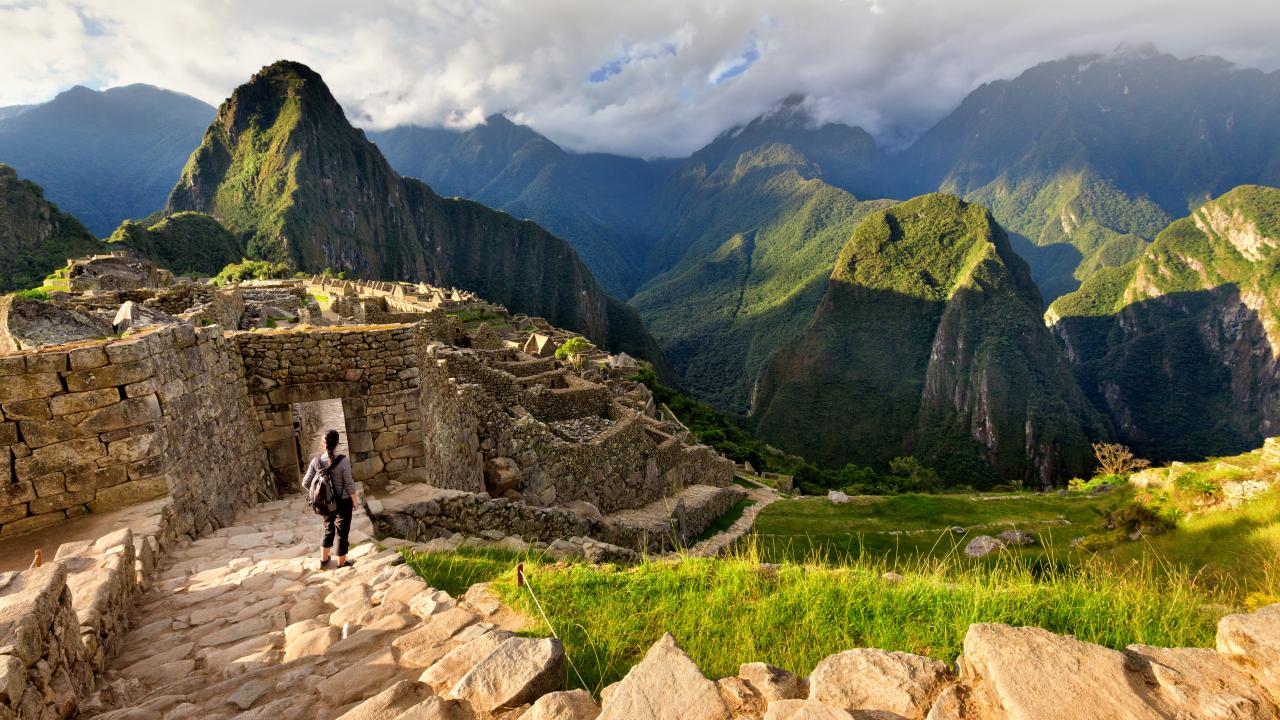 Back view of female tourist descending stairs overlooking Machu Picchu ruins at sunset, Peru